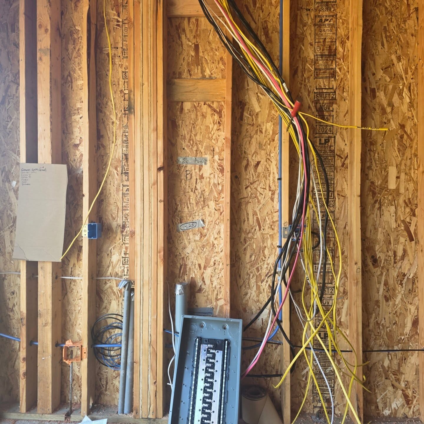 Color-coded conductors running down a new-construction stud wall to a service panel