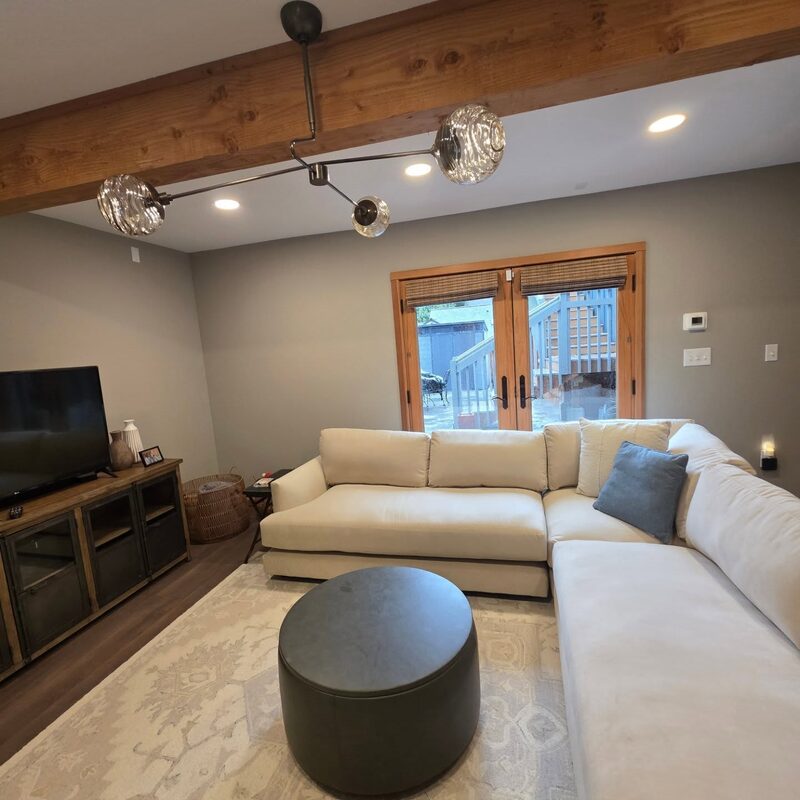Modern chandelier mounted on a wood ceiling beam in a finished living room