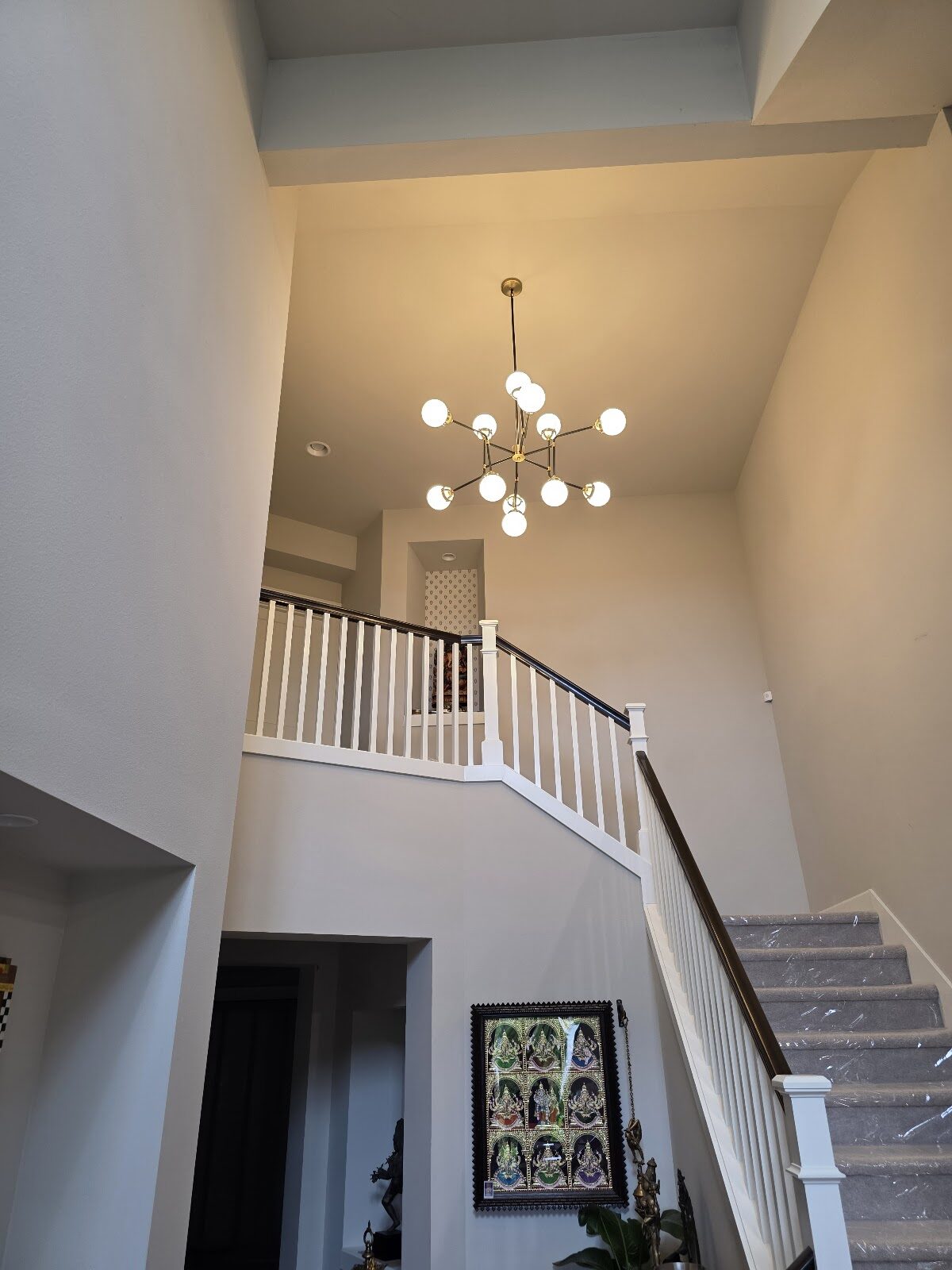 Finished brass globe chandelier centered over a two-story staircase foyer